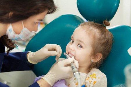 专业牙医在面膜抛光儿童牙齿与现代电动工具。 孩子在现代办公室磨牙的医疗过程中没有恐惧。