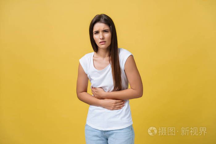 室内肖像的可爱女孩站在与交叉的手在腹部, 感觉尴尬或痛苦, 而在一旁