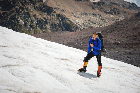 一个登山运动员带着背包走在轮椅上, 站在一座布满灰尘的冰川上, 手里拿着运动鞋在山上的裂缝之间。