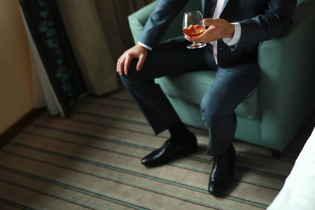 男人坐在椅子上，穿着时髦的西装，手里拿着一杯酒