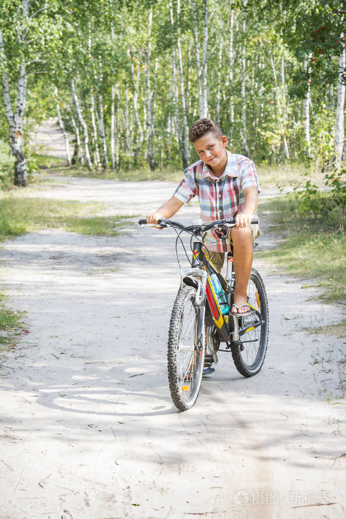 夏天,在树林里,路上骑着一个英俊的男孩骑着自行车.