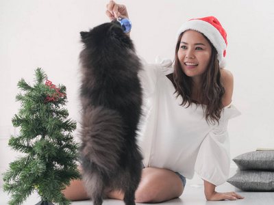 快乐的亚洲女人在圣诞树生活理念附近抚摸她的黑狗。