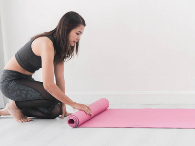 快乐亚洲运动女性滚动粉红色瑜伽垫在家里的生活方式概念。