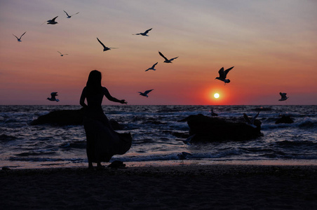 夏天在海滩上散步.一个女孩在日落背景日出上的剪影在海平线上.