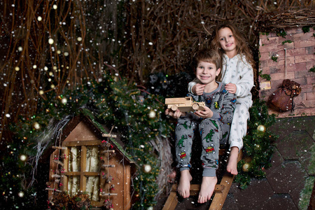 圣诞节，漂亮的孩子们坐在房子的屋顶上。 雪落在房子的屋顶上。 孩子们很快乐