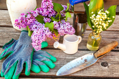 园艺工具浇水，可以铲铲，耙，手套，丁香百合的山谷花，在老式的木桌上。 春季或夏季园林生态自然园艺爱好概念