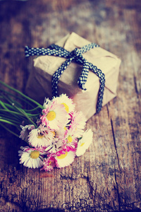 明亮的雏菊花束和木制桌子上带丝带的礼品盒