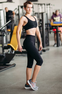 运动妇女与强壮的身体和短发站立在姿势在健身房