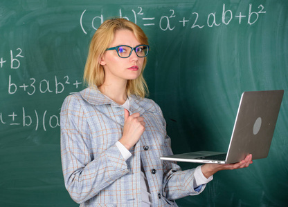 老师优雅的女士与现代笔记本电脑冲浪黑板背景。远程教育理念。女教师戴眼镜持有笔记本电脑上网。学校创新理念