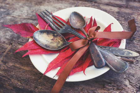 木桌上有秋叶和餐具的盘子特写