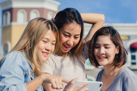 快乐的年轻亚洲青少年在城市,同时与她的朋友一起用智能手机拍摄自我