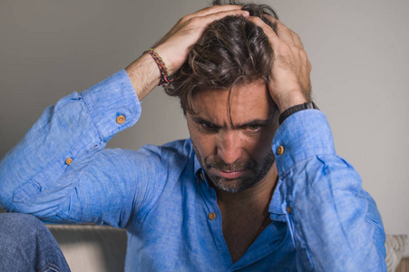 英俊,悲伤的拉丁男人,疲惫和沮丧地坐在家里的沙发上,感到不知所措和