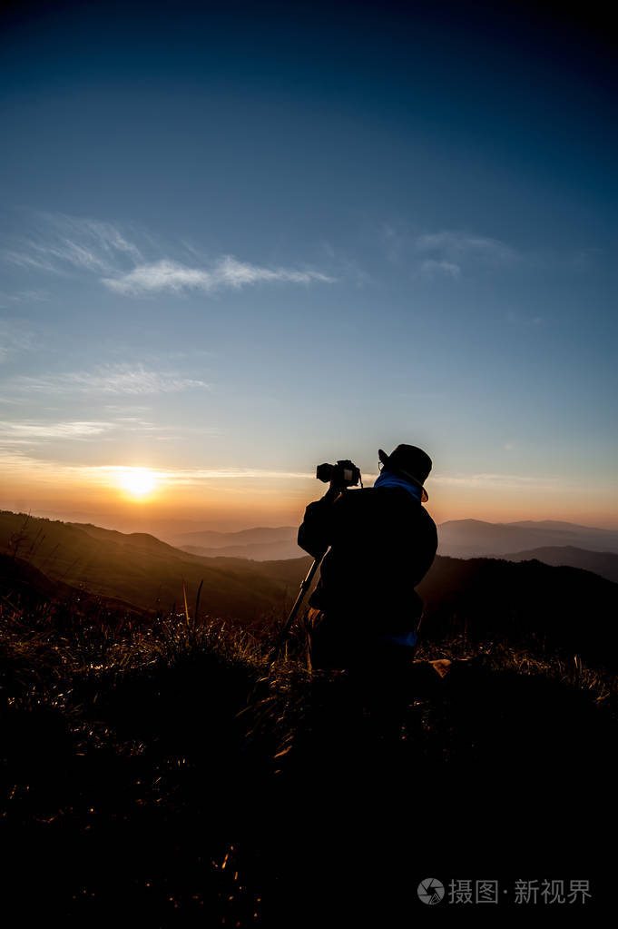 摄影师在日出时拍摄风景的剪影