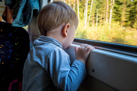 美丽的幼儿男孩看外面火车窗外, 而它移动。冬天乘火车去度假和旅游