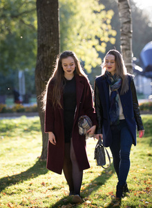 两个穿大衣的漂亮女孩走在秋天阳光明媚的公园里。