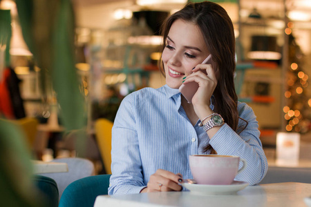 美丽可爱的白种女人在咖啡馆, 使用手机和喝咖啡微笑