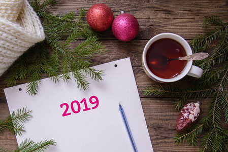 2019新年美丽的圣诞图片布局明信片一杯茶一个带笔的笔记本带玩具的杉木树枝木质乡村背景上的温暖围巾俯视图