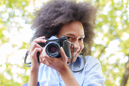 迷人的黑人妇女的肖像与旧的复古相机，女摄影师，户外非洲发型，穿休闲服装，看相机。