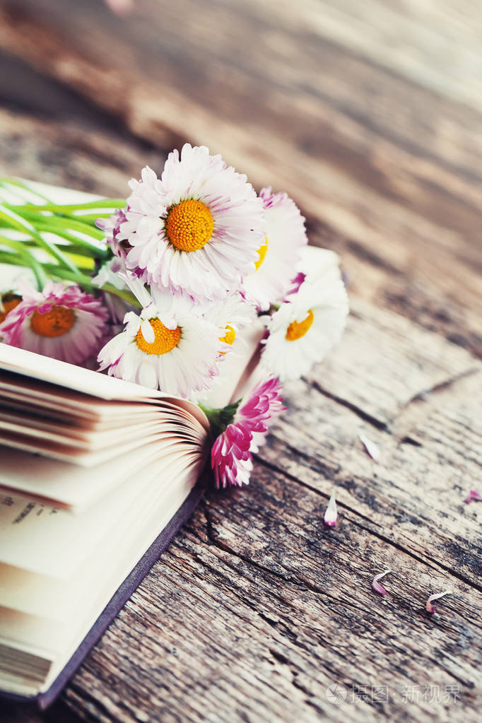 木制桌子上打开的书上放着鲜艳的雏菊花束