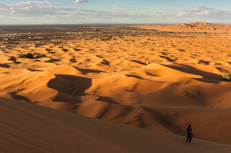 女孩站在沙丘上，观察默祖加摩洛哥的沙漠景观