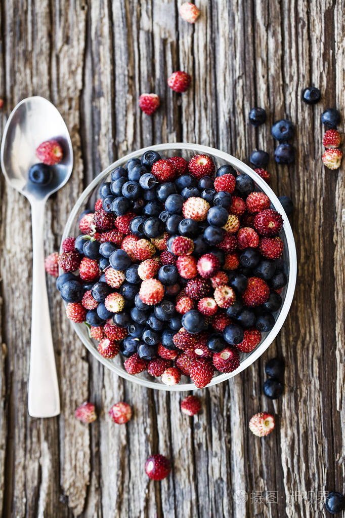 新鲜成熟的野生草莓和蓝莓放在木碗里用勺子