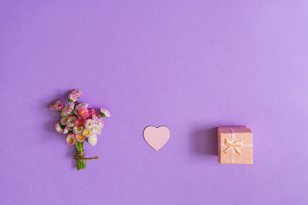 夏季创意作文以最小的风格。 白色和粉红色玛格丽特雏菊花束与心和礼品盒在淡紫色背景。 俯视图平面布局复制