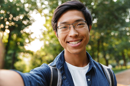 很高兴戴眼镜的亚洲男学生在户外自拍和看相机。