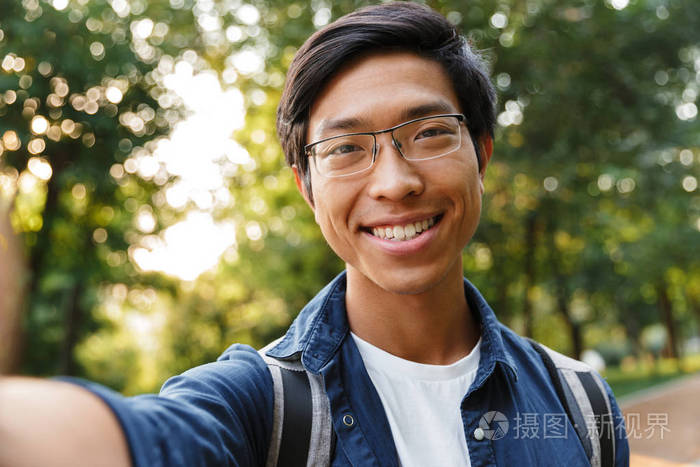 很高兴戴眼镜的亚洲男学生在户外自拍和看相机