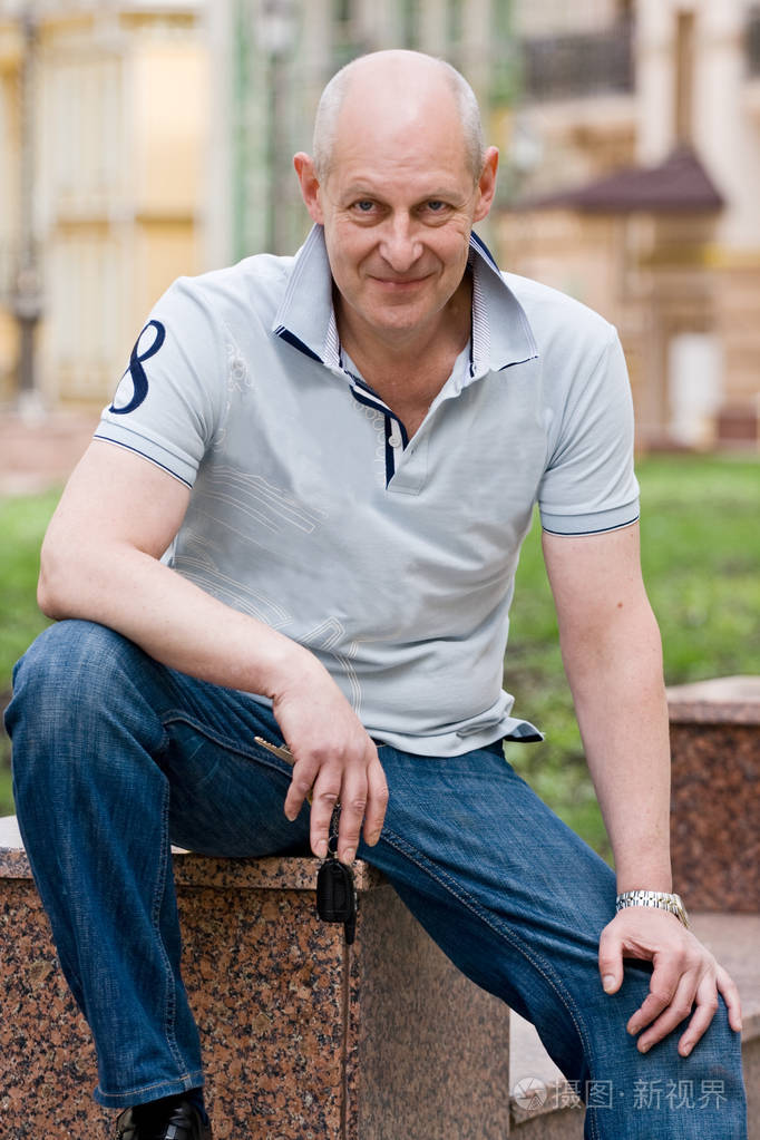 一个秃顶微笑的中年男人在一条城市街道上拿着一把汽车钥匙