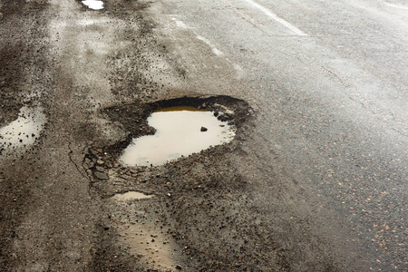 道路上铺着雪坑和水坑的裂缝. 阴天灰色天气下冬季道路的景观.