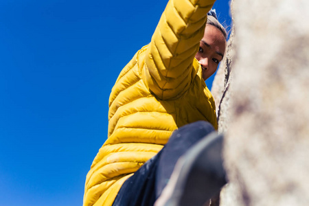 娇小的亚洲女人在户外攀岩时，穿着一件亮黄色的蓬松夹克，挂在石壁上