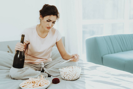 孤独的哭泣的女人看着床上的照片。 手里拿着一瓶香槟。 不愉快的假期。 悲伤的周末。 眼泪在脸上。 失望的女孩。 心情不好的女性。