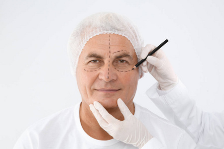 医生在白色背景的整容手术前给老人做面部标记