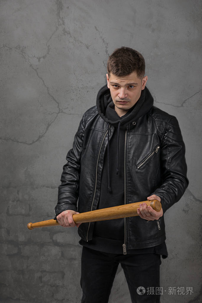 那个穿着黑色墙上皮夹克的年轻人用棒球棒摆出一副战斗姿势