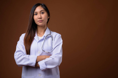 年轻美丽的亚洲妇女医生反对棕色背景
