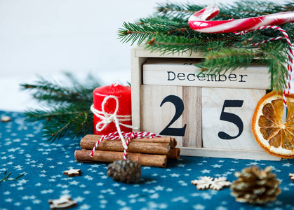 木制日历与12月25日的日期在绿色的地方垫蜡烛冷杉树干橙松树。 圣诞庆典明信片概念