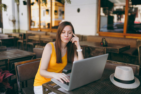 妇女在户外街头咖啡厅，坐在桌子上，工作在现代笔记本电脑电脑，在餐厅放松，在空闲时间。 夏天的移动办公室。 生活方式自由职业商业概