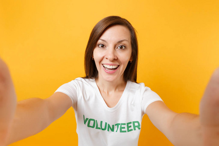 自拍的幸福微笑满意的女人在白色T恤与书面铭文绿色标题志愿者隔离在黄色背景。 自愿无偿援助慈善恩典工作概念
