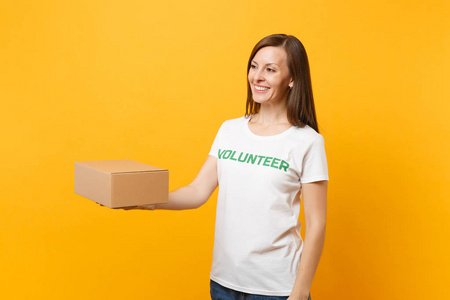 微笑的女人在白色T恤上的肖像，上面写着绿色标题，志愿者用黄色背景上孤立的空白纸板盒。 自愿免费援助帮助慈善恩典概念