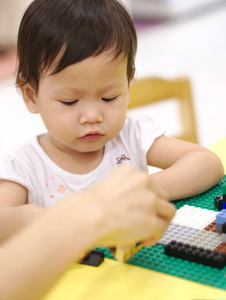 亚洲宝宝与家长在室内黄桌玩拼图玩具