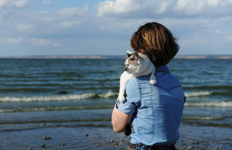 抱着一只白猫的女孩.阳光明媚的海洋和岛屿背景照片