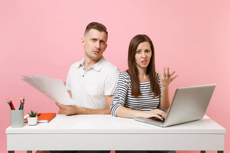 两位愤怒的年轻商务女性男性同事坐在白色办公桌前工作，现代笔记本电脑被隔离在粉彩背景上。成就职业概念。复制空间广告，青年合作