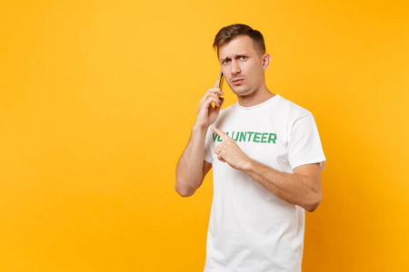 年轻人的肖像穿着白色T恤，上面写着绿色的标题，志愿者在手机上交谈，在黄色的背景上被隔离。 自愿无偿援助慈善恩典工作概念