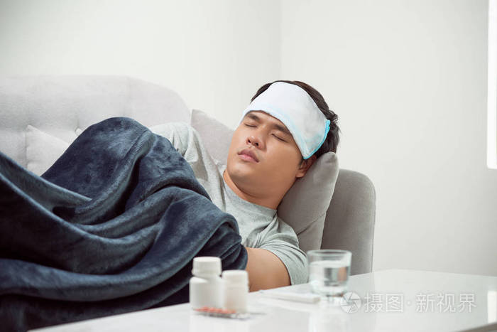 躺在沙发上患感冒和冬季流感病毒的病人在保健观念中服用药片看温度计