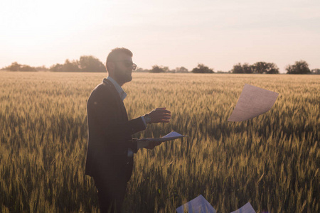 一位年轻的商人把一张纸扔到空中的肖像，日落于夏日的田野背景