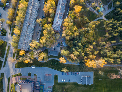 在阳光明媚的秋日日落时分，在一个停车场上悬挂着五层楼房的空中俯瞰着市中心的高大树木，树上有绿色和黄色的叶子，还有汽车