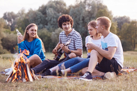 喝酒唱歌水平拍摄的友好的年轻人有快乐的表情,在周末一起坐在篝火旁