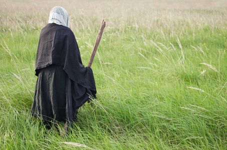 邪恶的老巫婆弓着腰在高高的草地上拿着扫帚照片