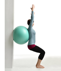 女健身教练在健身房举行腿和运动腹部与绿色体育球在白色