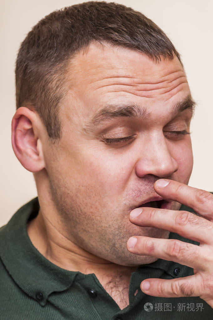 年轻疲惫的打哈欠的人捂住张开的嘴.